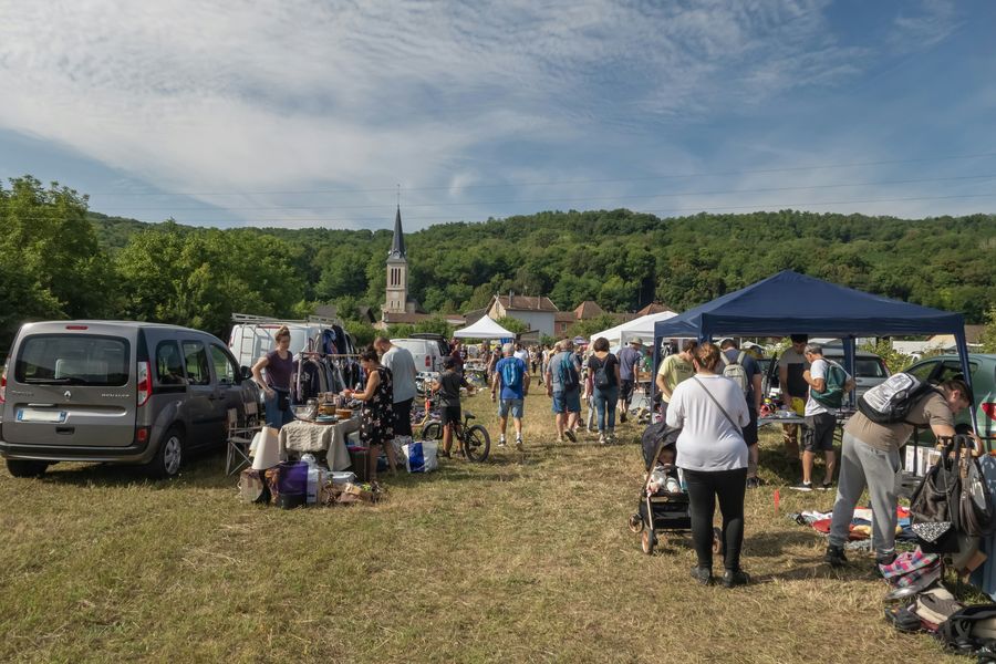 Car boot sale in a field, with sellers' vans, trestle tables of goods and a church spire behind