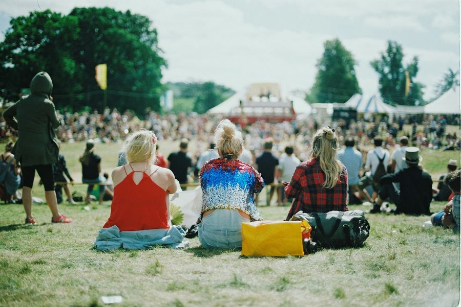 Festival-goers sitting on the grass watching a distant stage at a summer event