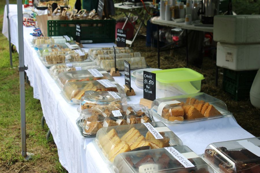 Cake stall at a village fete, with boxed sponge cakes on a trestle table and handwritten price signs